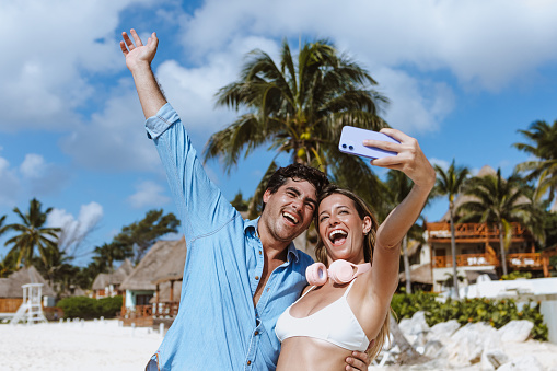 hispanic young couple taking photo selfie on beach vacations or holidays in Mexico Latin America, Caribbean and tropical destination