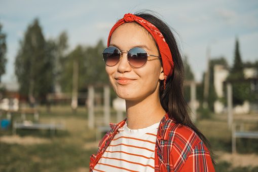 Summer lifestyle portrait of a smiling stylish young woman in sunglasses at sunset outdoors. Student girl walks around the university campus on a sunny summer day