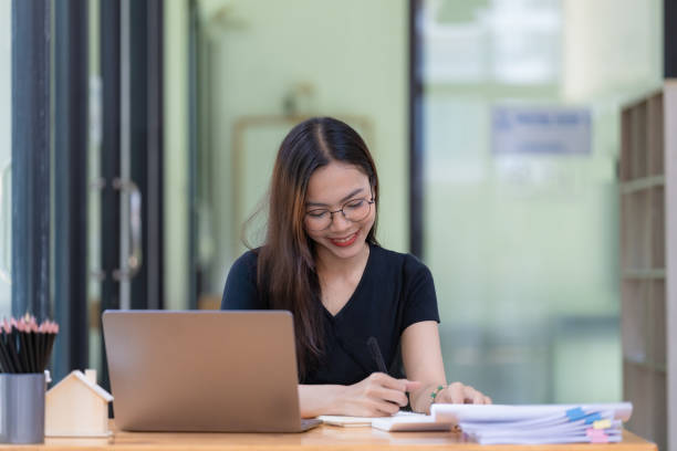 istock A beautiful young Asian businesswoman is saving and checking work and documents with her laptop computer at her desk with a bright smile on her face. 1506592010