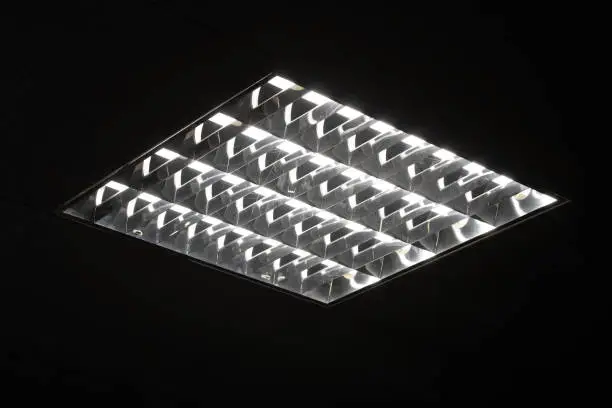 Photo of Fluorescent lamps in square lampshade in dark room.