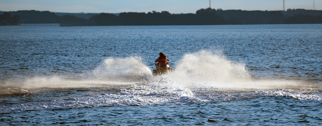 A monitor and a girl or father and daughter enjoying and having a good time on the jet ski skidding at high speed creating foam in the water of Boiro beach against the light heading towards the coast