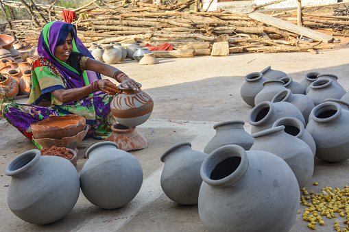 TIKAMGARH, MADHYA PRADESH, INDIA - AUGUST 13, 2022: Portrait of happy traditional Indian woman potter artist painting on clay pot for sale.
