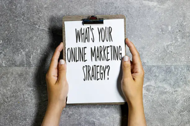 Photo of closeup hands holding a paper clipboard with Whats Your Online Marketing Strategy? concept