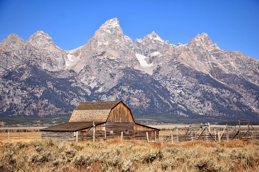 A rustic old barn in a lush green meadow, with a scenic mountain backdrop in the distance