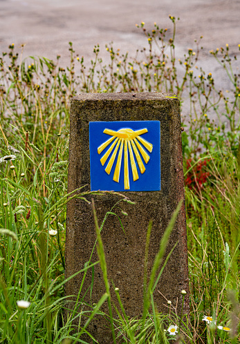 Camino de Santigo milestone, information sign camino del norte, Sobrado, A Coruña province,  Galicia, Spain. Scallop tile, pilgrimage symbol and yellow arrow . Copy space on the left.