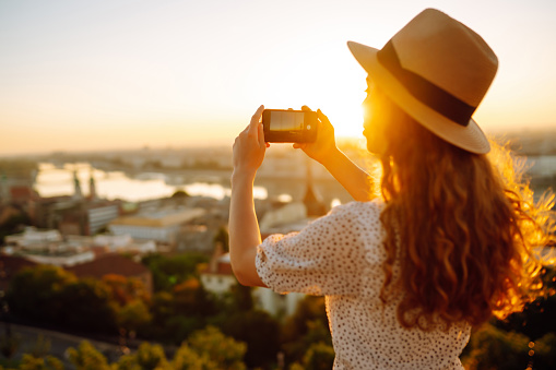 Tourist woman shoots a city landscape at dawn on a smartphone.