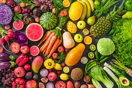 Colorful raw fruits and vegetables varied vegan food, vivid rainbow arrangement full frame background