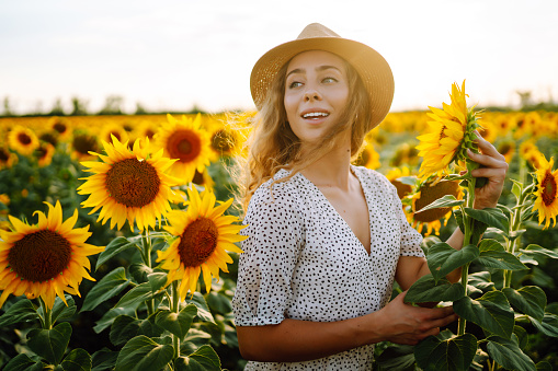 Beautiful woman strolling through field with sunflowers. Fashion, lifestyle, travel and vacations concept.