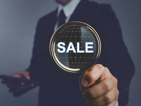 Businessman holding a magnifying glass with sale text. Searching for discounted items from the internet worldwide.