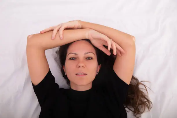 Woman with vitiligo skin condition lying in bed with her arms crossed above her head