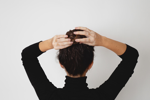 Woman with vitiligo pulling out a hair bun. Rear view