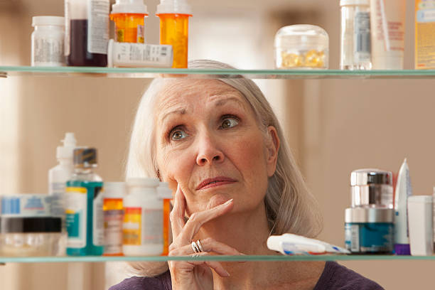 старший женщина, глядя через домашняя аптечка - medicine cabinet prescription pill bottle medicine стоковые фото и изображения