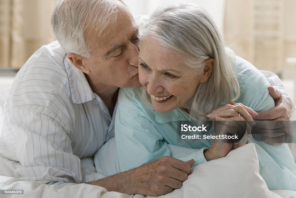 Senior homme Embrasser femme au lit - Photo de 65-69 ans libre de droits