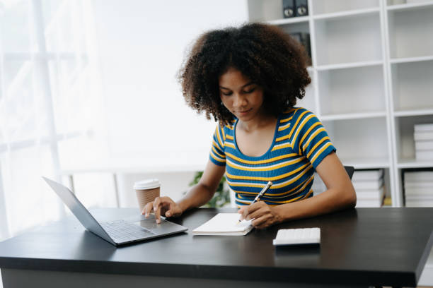istock Beautiful African woman using laptop and tablet while sitting at her working place. Concentrated at work in home office 1506846712