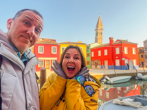 Very handsome mid adult hetersexual man and beautiful woman smiling and looking at camera. Happy real people. Travel destination background, copy space. Honeymoon just married husband and wife posing at Burano island in Venetian lagoon.