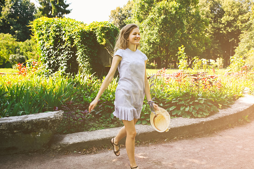 Beautiful girl in stylish hipster dress and hat is jumping in the park. Summer happy photoshoot outdoors.