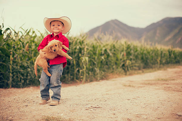 A young boy holds is golden retriever puppy while on the farm.