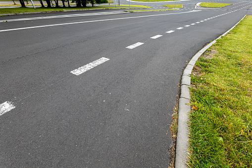 Road marking system. line on the asphalt. concrete curb and lawn. Roundabout in the background.