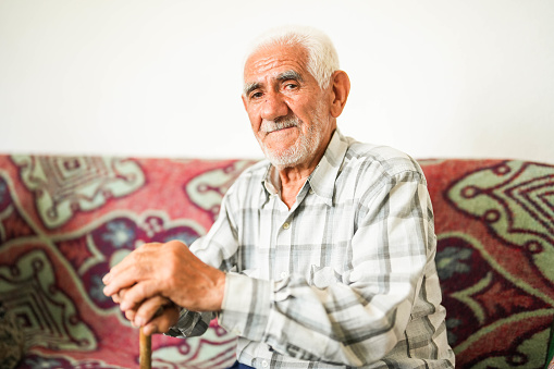 white haired senior man sitting on sofa holding walking stick