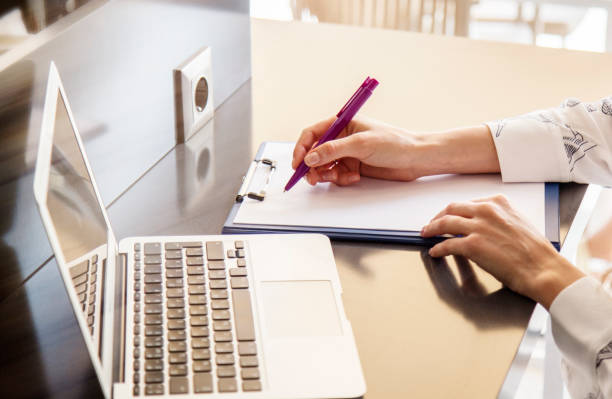 istock Hands of a young woman writing text on a clipboard and using laptop 1506982928