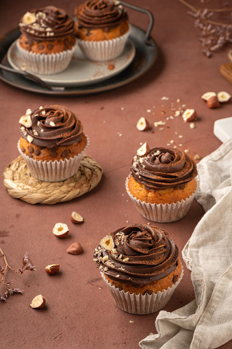 Chocolate chip muffins decorated with chocolate ganache and hazelnut on a kitchen countertop.