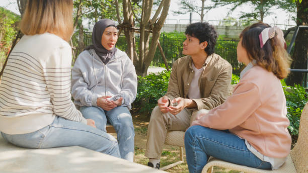 Small Asian group of people sit in a close circle and talk to a therapist in park. Smile people sharing story happy speak diverse people sitting in circle at group therapy session psychologist. stock photo
