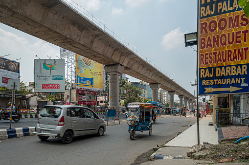 Kolkata, India - 25th March 2023: Traffic on the busy Biswa Bangla Sarawi, an arterial highway through Rajarhat, New Town in West Kolkata, India. The overhead metro train system was under construction at the time of photographing.
