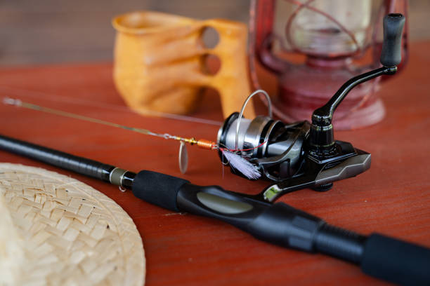 Close-up of spinning rod, straw hat, lantern and mug on wooden table