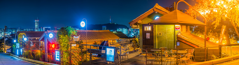 Fairy lights illuminated pavement cafes in the Ihwa Mural Village beside Naksan Park overlooked by Namsam Tower in the heart of Seoul at night, South Korea’s vibrant capital city.
