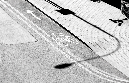 Shadows and road markings on city street, bike lane and sidewalk in black and white, from above