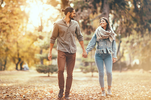 Beautiful smiling couple is enjoying in sunny city park in autumn colors looking each other.