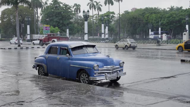 Havana, Cuba; October 2022: Rain in Cuba, water pouring over a vintage retro blue car in Havana Street - Storm Season in Cuba