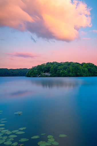 Sunset and dramatic cloudscape over the lake with green forest, water lilies, and reflections at Lincoln State Park in Providence, Rhode Island
