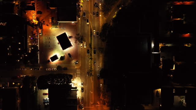 Top down view of traffic in streets in night city. Vehicles driving on road illuminated by streetlights.