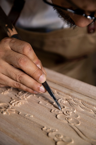 An old Chinese carpenter is carving words on a wooden board, traditional technique, indoor shooting, partial close-up(Translation: The carved text reads \