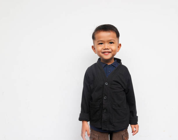 A smiling toddler boy standing while looks at the camera with confidence, isolated on white background