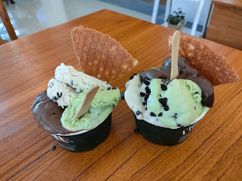 You can see two glasses of gelato ice cream served on the table. one glass of gelato ice cream has three flavors, namely chocolate, green tea, and choco vanilla. at the top there is a distinctive sweet crunchy crackers.