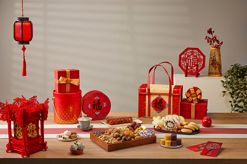 Chinese style festive atmosphere, wooden dining table, various snacks, pastries, lanterns, gifts, red envelopes, fish, Chinese food, dumplings(Translation:The text means auspicious and good luck)