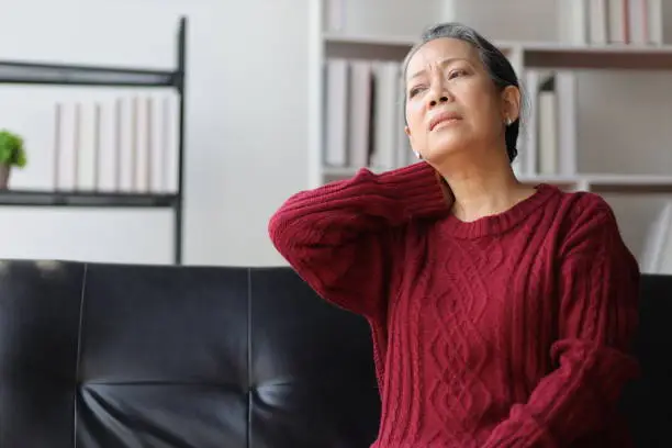 Photo of Senior woman sitting on the sofa at home is sick and has neck pain.