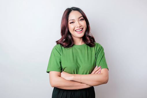 Portrait of a confident smiling Asian woman standing with arms folded and looking at the camera isolated over white background