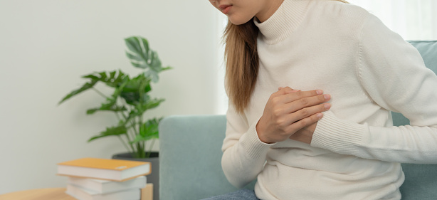 hand hold chest with heart attack symptoms, asian woman have chest pain caused by heart disease, leak, dilatation, enlarged coronary heart, press on the chest with a painful expression