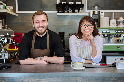 Colleagues, partners, smiling man and woman looking at camera, in coffee shop near counter. Team, small business, work, staff, cafe cafeteria restaurant, entrepreneurship concept