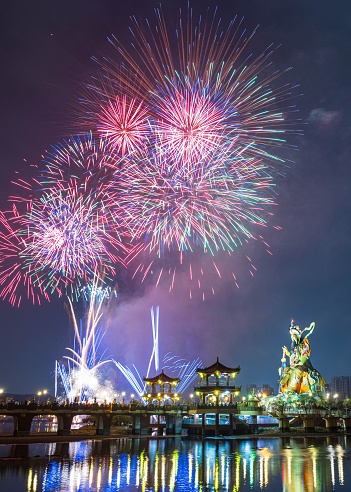 Fireworks exploding in the night sky above a river, surrounded by a bridge leading to a dragon sculpture
