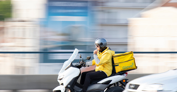 Belgrade, Serbia - May 20, 2023: Courier service delivery person working for Glovo riding a scooter with rear container in city traffic