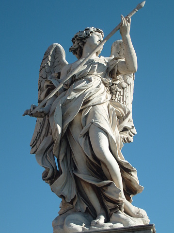 The detail of one of the monumental statues of angels along the Ponte Sant'Angelo (Saint Angel bridge), in the historic and baroque heart of Rome. This bridge was built under the emperor Hadrian in 134 AD. to connect the heart of Rome with his mausoleum, currently Castel Sant'Angelo. A few centuries later, under the pontificate of Pope Clement IX, the architect and sculptor Giovanni Lorenzo Bernini was commissioned to create the current balustrade decorated with ten statues of the Angels of the Passion of Christ. According to the Christian tradition, each Angel holds one of the relics of the Passion of Christ, such as the cross, the veil of Veronica, the nails, the spear, the pillar of the scourging, etc. Designed by Bernini, the statues were made under his direction in 1669 by the pupils present in his school of sculpture. In 1980 the historic center of Rome was declared a World Heritage Site by Unesco. Image in high definition image.