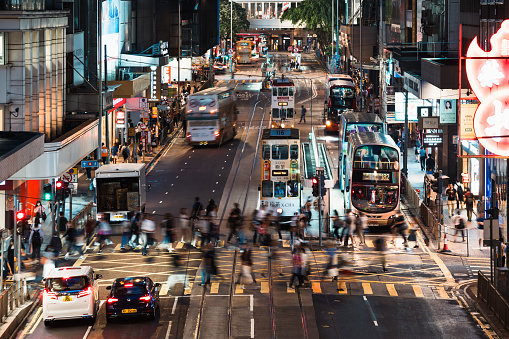 Motion blur of Chinese people, crowd Asian commuter walk cross road, car, bus, taxi traffic transportation at Hong Kong Central district at night. Asia transport lifestyle, or urban city life concept