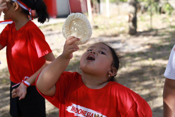 niños indonesios celebran el día de la independencia de indonesia con un concurso al aire libre - eating child cracker asia fotografías e imágenes de stock