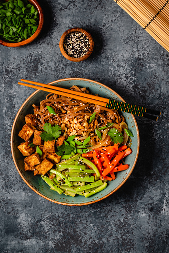 Soba noodles with vegetables and fried tofu in a bowl. Top view.