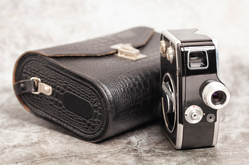 Vintage movie camera with filters and crocodile skin case on a gray background.