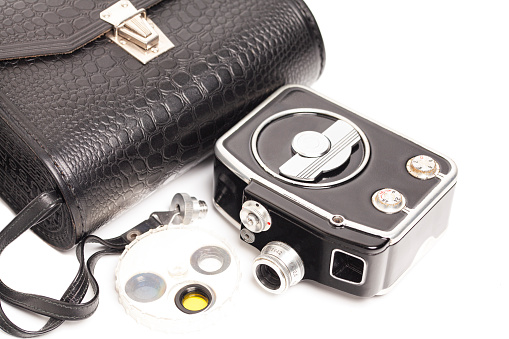 Vintage movie camera with filters and crocodile skin case isolated on white.